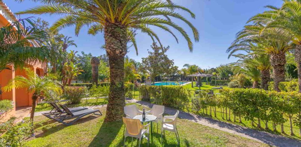Jardín con mesa y sillas bajo palmeras junto a la habitación familiar grande del hotel.