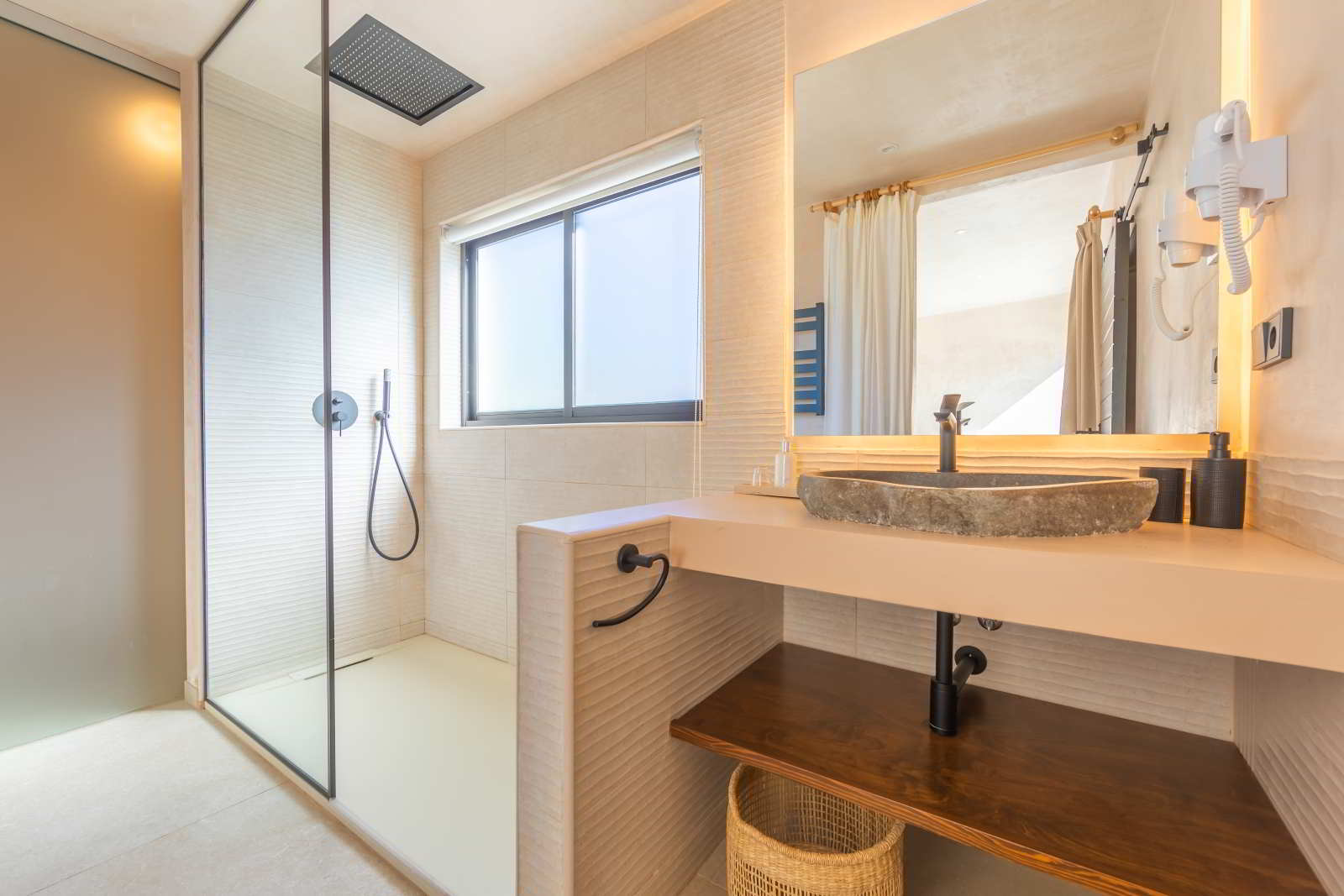 Baño con ducha acristalada, lavabo de piedra y espejo con luz indirecta en La Villa del Hotel Punta Sur.
