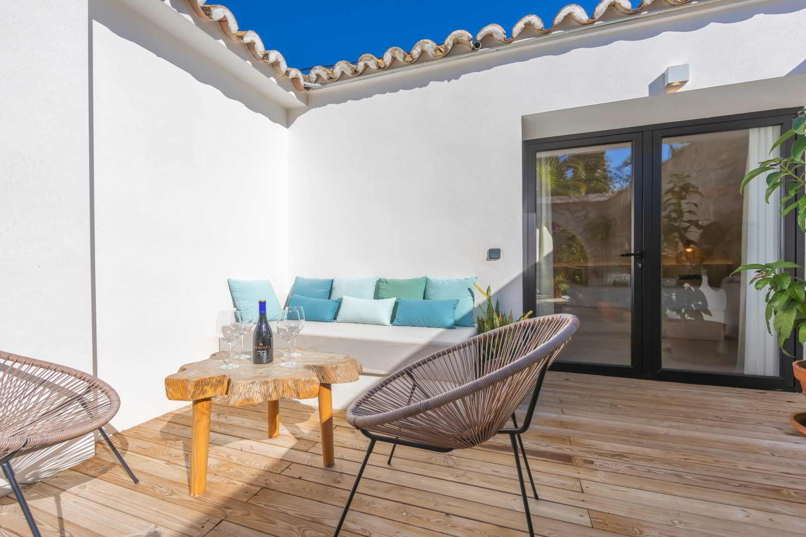 Zona de estar exterior en La Villa del Hotel Punta Sur con sofá integrado, cojines en tonos turquesa y mesa rústica con vino.