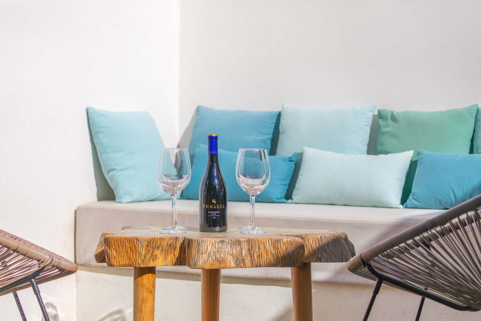 Detalle de terraza en La Villa del Hotel Punta Sur con mesa de madera, dos copas de vino y un sofá con cojines en tonos azules.