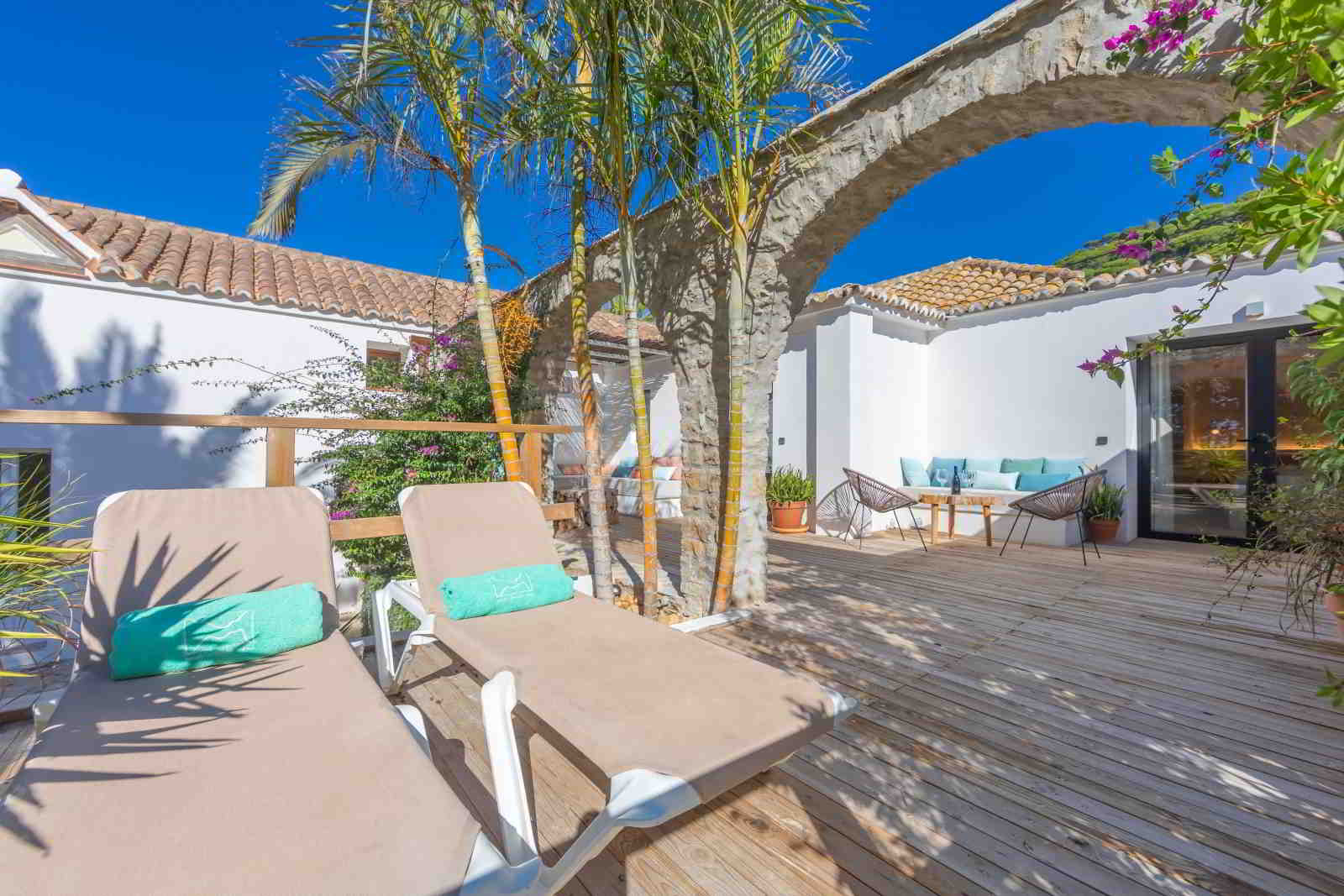 Terraza de madera en La Villa del Hotel Punta Sur con tumbonas, sofás exteriores, arcos de piedra y vegetación tropical.