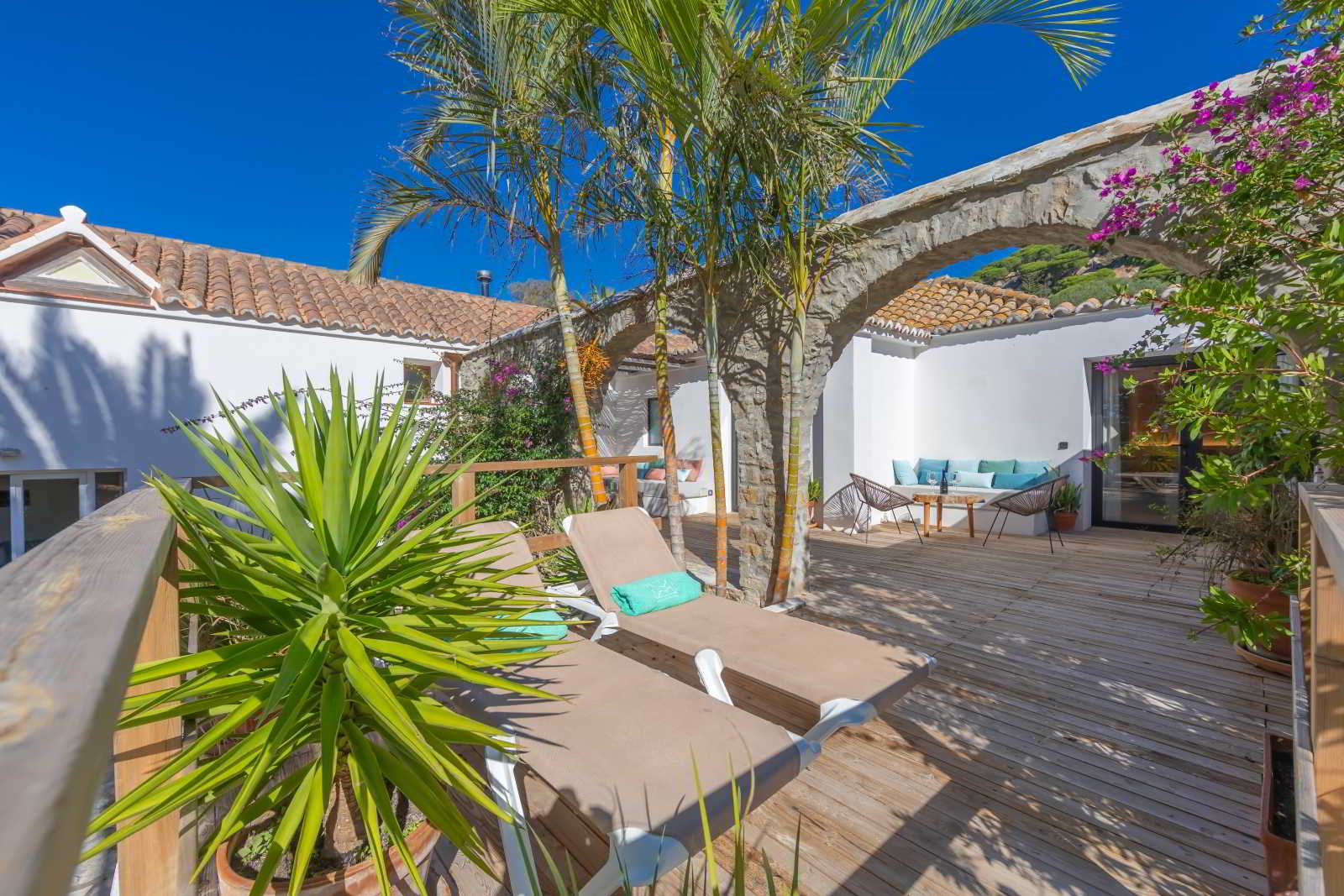 Terraza de La Villa en Hotel Punta Sur con tumbonas, sofá exterior, palmeras y detalles arquitectónicos de piedra bajo un cielo despejado.