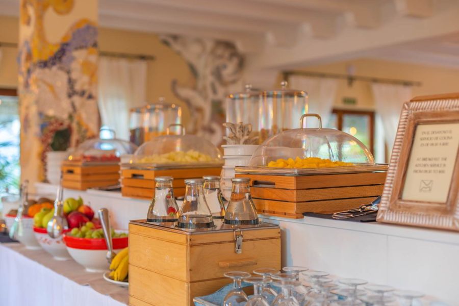 Vista general del buffet de desayuno del Hotel Punta Sur con fruta cortada, cereales, aguas y utensilios de autoservicio.