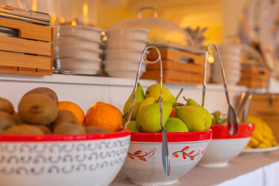 Frutas frescas como peras, kiwis y naranjas en boles de cerámica decorada en el bufé del Hotel Punta Sur.