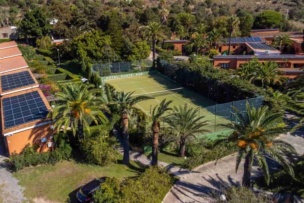 Vista aérea del Hotel Punta Sur con pista de tenis, jardines tropicales y edificios de estilo andaluz entre palmeras.