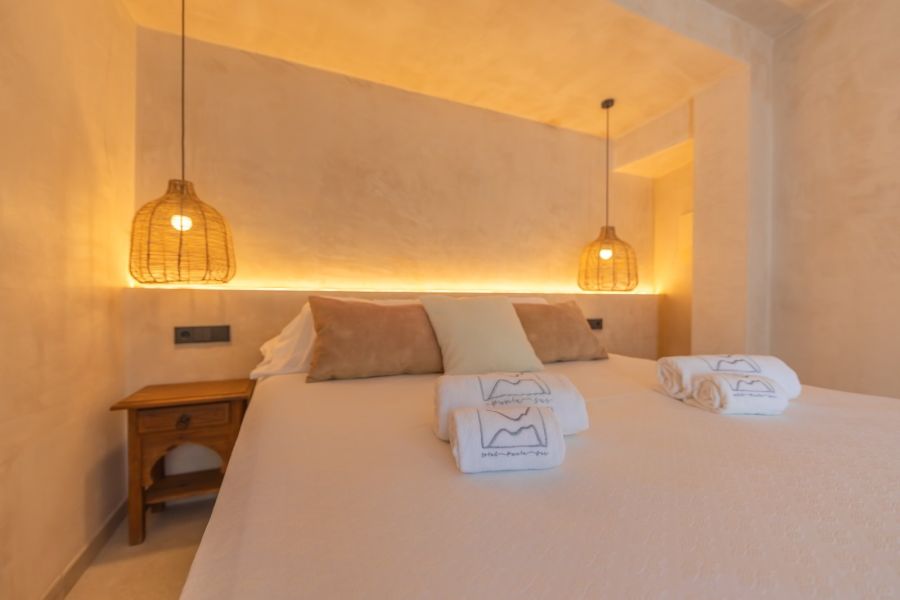 Cama doble en La Villa del Hotel Punta Sur con iluminación cálida, cojines en tonos neutros y lámparas de mimbre colgantes.